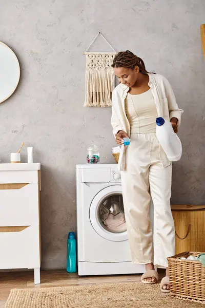 Eine afroamerikanische Frau steht in einem Badezimmer vor einer Waschmaschine und wäscht ihre Wäsche. — Stockfoto