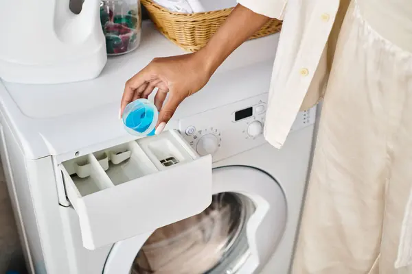 Femme afro-américaine nettoie une machine à laver dans une salle de bain dans le cadre de sa routine de ménage. — Photo de stock