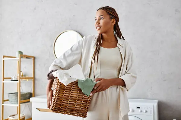 An African American woman with afro braids gracefully holds a basket in a room while doing laundry. — Stock Photo