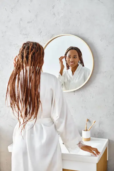Eine afroamerikanische Frau mit Afro-Zöpfen bürstet sich in einem modernen Badezimmer die Haare und konzentriert sich dabei auf Schönheit und Hygiene. — Stockfoto