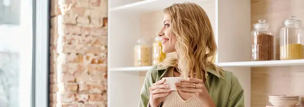 A woman standing in a kitchen while holding a cup. — Stock Photo