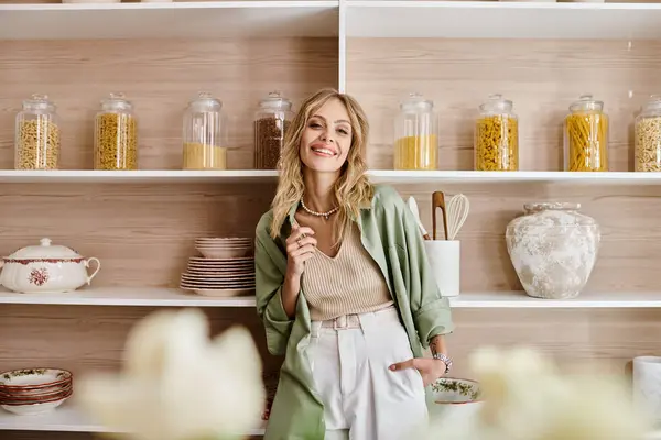 Woman in kitchen stands near shelf with many jars. — Stock Photo