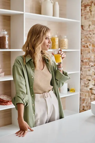Женщина, стоящая на кухне, держа стакан апельсинового сока. — стоковое фото