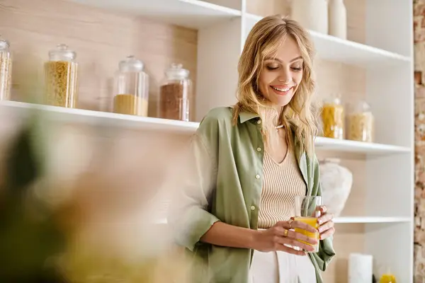 Une femme se tient devant une étagère dans une cuisine, tenant un fruit. — Photo de stock