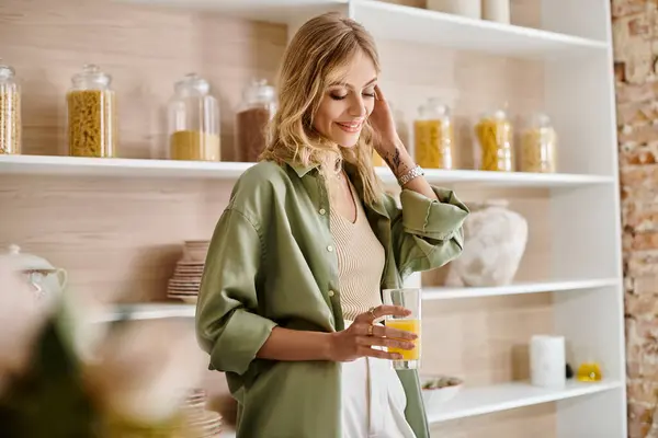 Donna in piedi in cucina con un bicchiere di succo d'arancia. — Foto stock