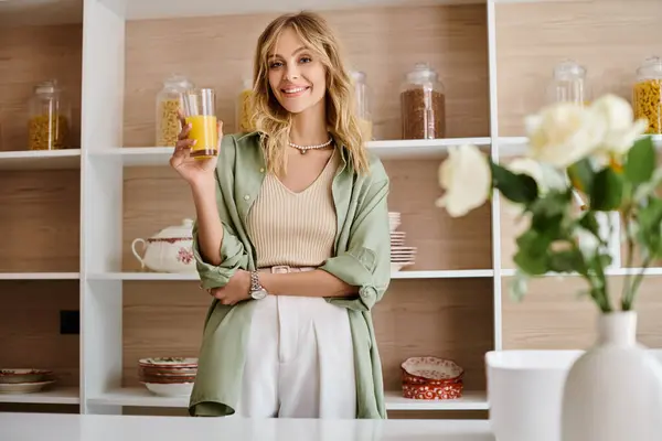 Uma mulher de pé em uma cozinha segurando um copo de suco de laranja. — Fotografia de Stock