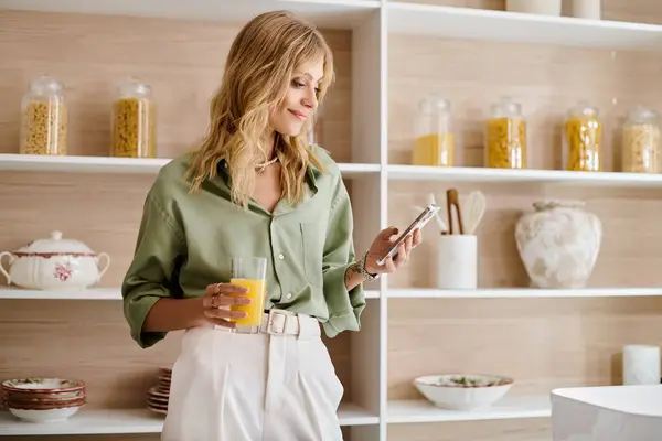 Frau steht in Küche und hält Handy vor Regal. — Stockfoto