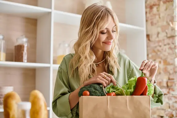 Woman holds full paper bag of fresh vegetables in kitchen at home. — Stock Photo