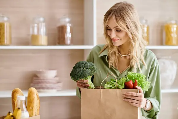 Mujer sosteniendo una bolsa de papel llena de verduras frescas en una cocina en casa. - foto de stock
