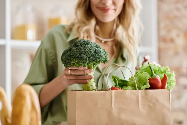 Une femme tenant un sac en papier rempli de divers légumes frais dans une cuisine. — Photo de stock