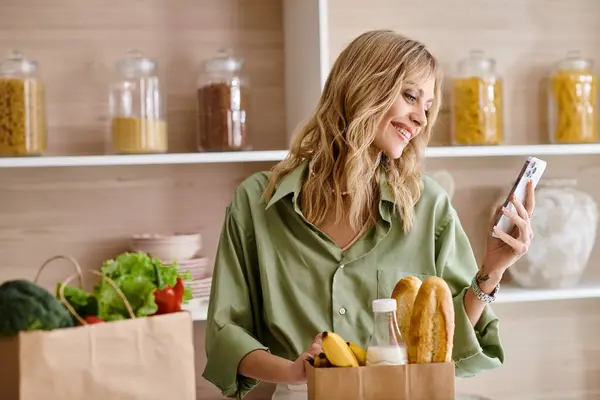 A woman in an apartment holding a bag of food and a cell phone. — Stock Photo