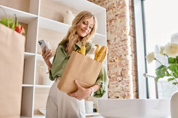 Una mujer sosteniendo una bolsa de papel llena de papas fritas en un entorno de cocina en casa. - foto de stock