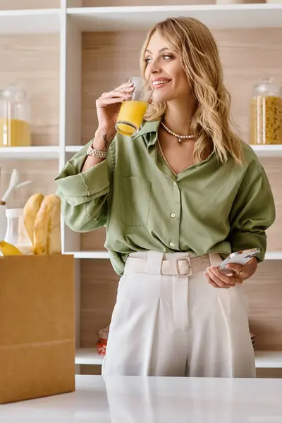 Eine Frau steht in einer Küche und trinkt ein Glas Orangensaft. — Stockfoto