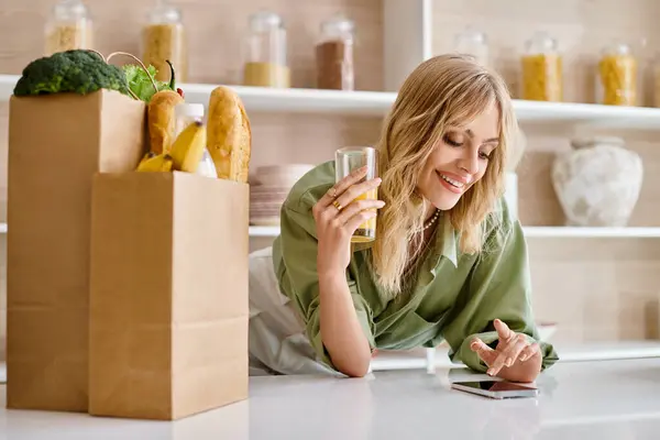 Une femme assise à une table dans une cuisine, concentrée sur son téléphone portable. — Photo de stock