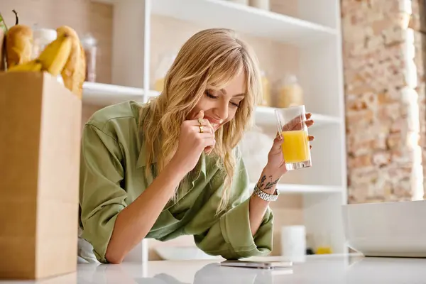 Una mujer en una cocina bebiendo un vaso de jugo de naranja. - foto de stock