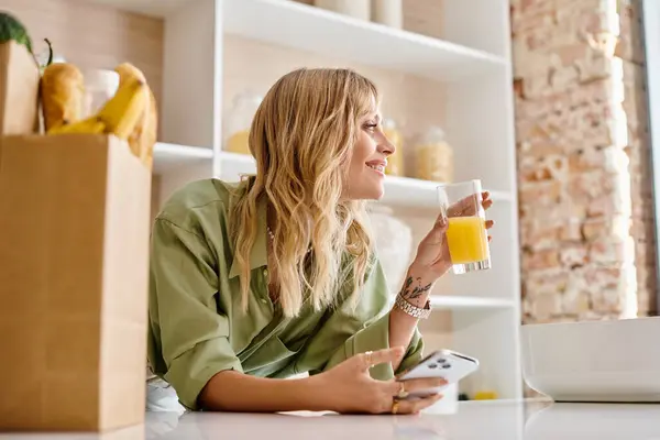 Una donna si siede a un tavolo da cucina con un bicchiere di succo d'arancia. — Foto stock