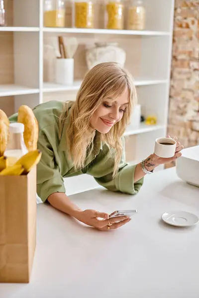 Une femme penchée sur une table, tenant une tasse de café dans un cadre de cuisine. — Photo de stock