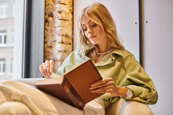 A woman sitting on a couch absorbed in a book in a cozy apartment. — Stock Photo