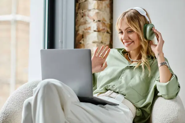 Una mujer en una silla trabajando en un portátil con auriculares. - foto de stock