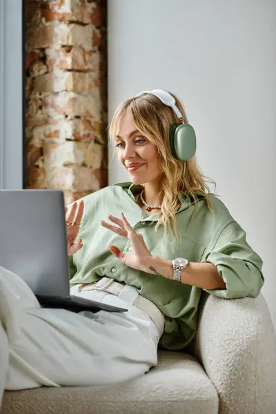 A woman in headphones sitting on a couch in a cozy apartment. — Stock Photo