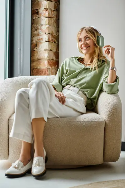 Une femme assise sur un canapé à côté d'une fenêtre dans un décor de maison ou d'appartement. — Photo de stock
