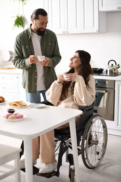 Веселая красивая инвалидная женщина в инвалидной коляске наслаждается кофе с мужем во время завтрака — стоковое фото