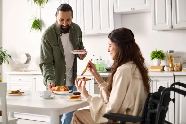 Щаслива приваблива жінка з інвалідністю в інвалідному візку їсть сніданок зі своїм люблячим чоловіком — стокове фото