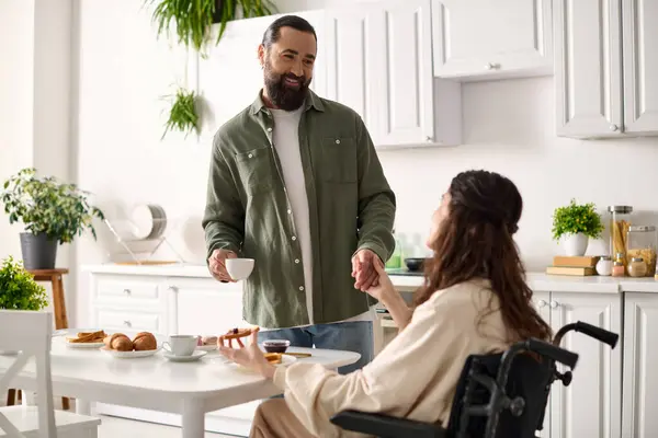 Радісна приваблива жінка з інвалідністю в інвалідному візку їсть сніданок зі своїм люблячим чоловіком — стокове фото