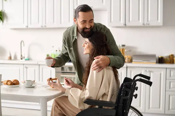 Радісна приваблива жінка з інвалідністю в інвалідному візку їсть сніданок зі своїм люблячим чоловіком — стокове фото