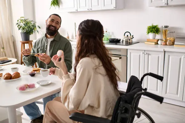 Fröhliche Frau mit Inklusivität im Rollstuhl beim Frühstück mit ihrem hübschen Mann Süßigkeiten essen — Stockfoto