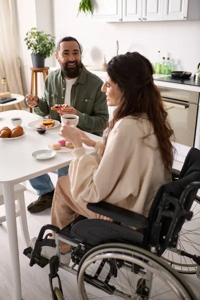 Joyful woman with inclusivity in wheelchair eating sweets at breakfast with her handsome husband — Stock Photo