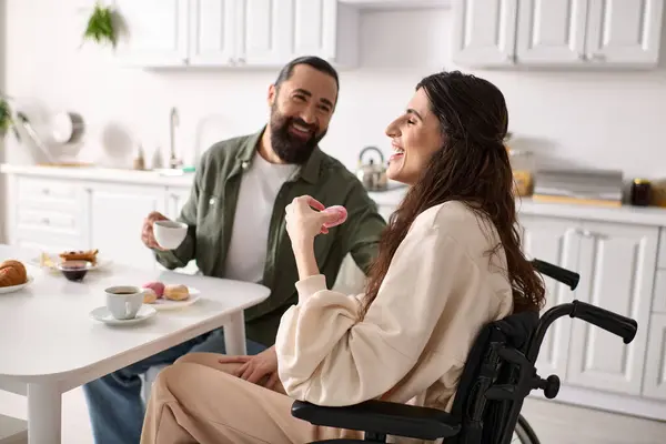 Mulher alegre com inclusividade em cadeira de rodas comer doces no café da manhã com seu marido bonito — Fotografia de Stock