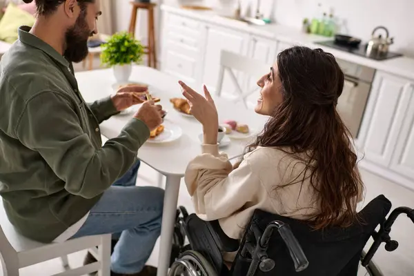 Красивый веселый мужчина, наслаждающийся завтраком с веселой женой-инвалидом в инвалидной коляске на завтраке — стоковое фото