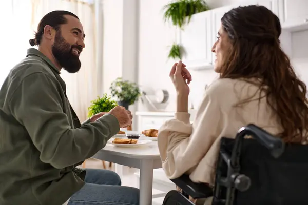 Beau joyeux homme appréciant le petit déjeuner avec sa femme heureuse handicapée en fauteuil roulant au petit déjeuner — Photo de stock