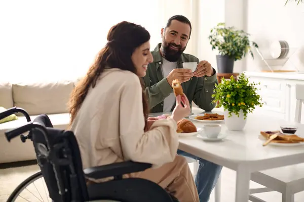 Positive man having great time at breakfast with his beautiful disabled wife that eating croissant — Stock Photo