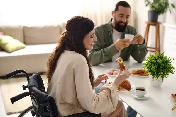 Hombre positivo pasar un buen rato en el desayuno con su hermosa esposa discapacitada que comer croissant - foto de stock