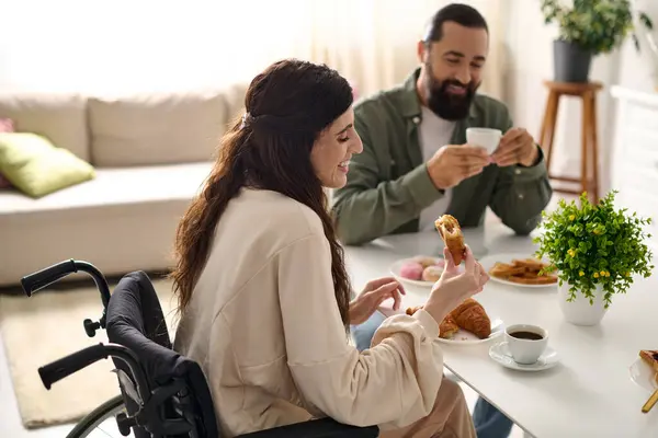 Positive man having great time at breakfast with his beautiful disabled wife that eating croissant — Stock Photo