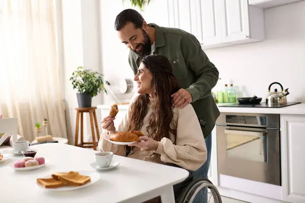Cheerful man having great time at breakfast with his beautiful disabled wife that eating croissant — Stock Photo