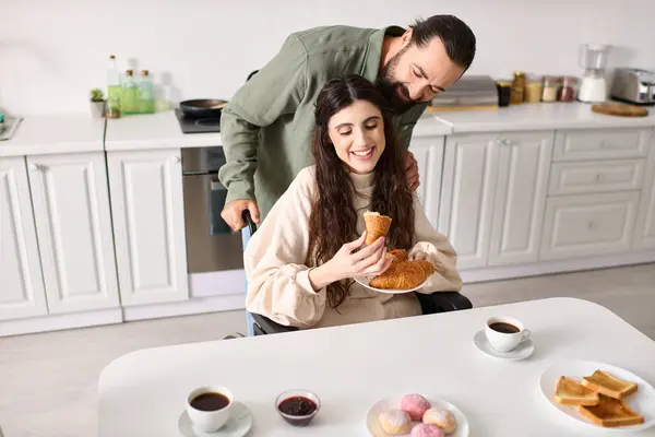 Uomo gioioso avendo grande momento a colazione con la sua bella moglie disabile che mangiare croissant — Foto stock