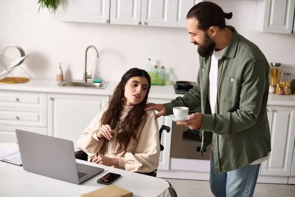 Bearded man in homewear offering coffee to his disabled hard working beautiful wife in wheelchair — Stock Photo