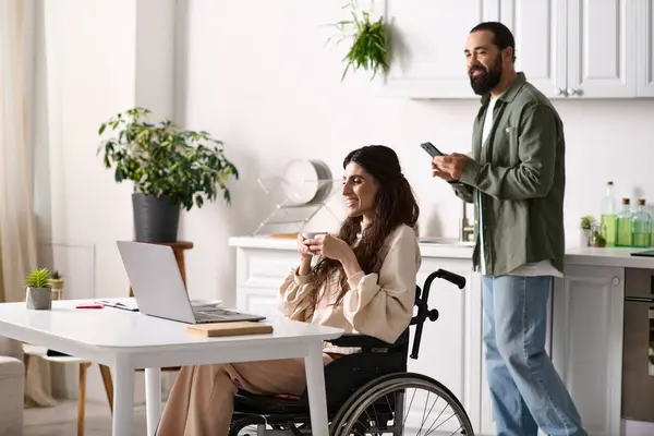 Hübsche behinderte Frau im Rollstuhl, die in der Nähe ihres Mannes arbeitet und auf das Telefon im Hintergrund schaut — Stockfoto