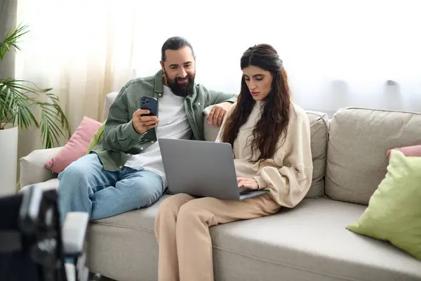 Красивая женщина с ограниченной подвижностью сидит на диване с ноутбуком рядом с мужем с телефоном — стоковое фото