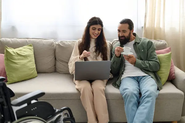 Homem barbudo alegre passar tempo de qualidade no laptop com sua bela esposa deficiente, beber café — Fotografia de Stock