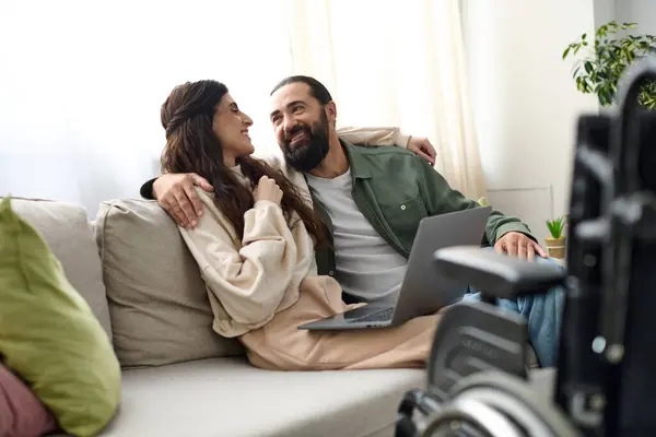 Loving couple of bearded man and disabled beautiful wife spending time together at laptop on sofa — Stock Photo