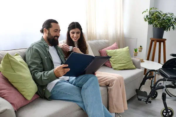 Gioioso uomo barbuto trascorrere del tempo di qualità al computer portatile con la sua bella moglie disabile, bere caffè — Foto stock