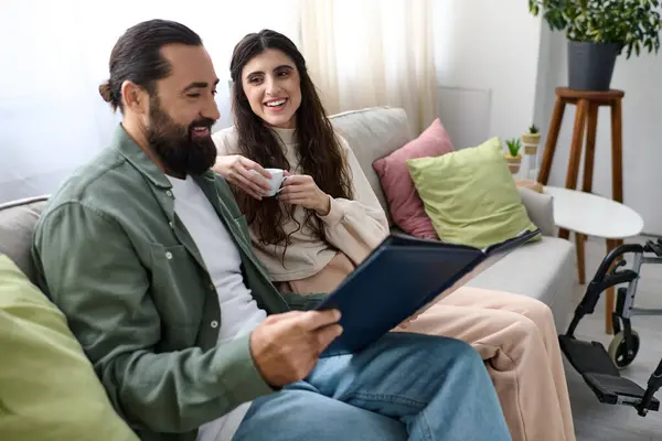 Веселый бородатый мужчина проводит время за ноутбуком со своей прекрасной женой-инвалидом, пьет кофе — стоковое фото