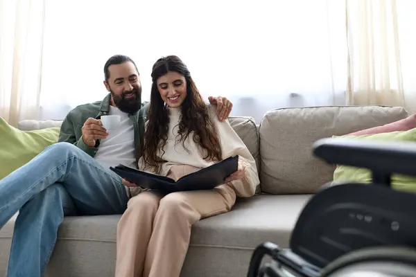 Joyous bearded man spending quality time at laptop with his disabled beautiful wife, drinking coffee — Stock Photo