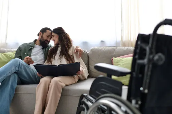 Joyous bearded man spending quality time at laptop with his disabled beautiful wife, drinking coffee — Stock Photo