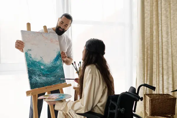 Красива жінка з інвалідністю малює на мольберті поруч зі своїм веселим бородатим чоловіком — стокове фото