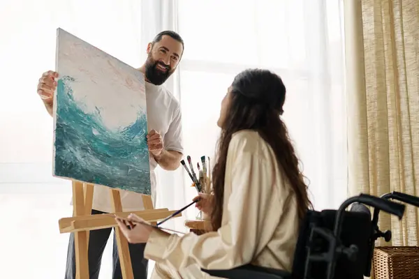 Beautiful woman with mobility disability painting on easel next to her cheerful bearded husband — Stock Photo
